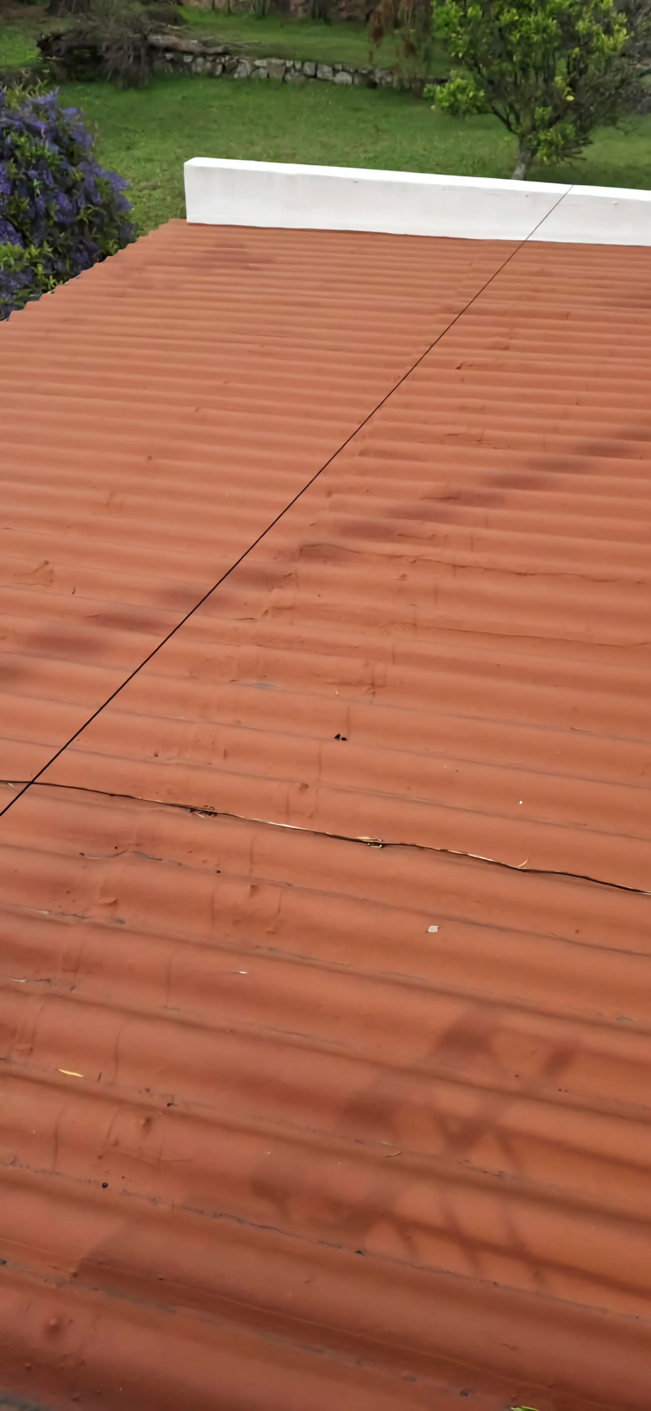 A corrugated sheeted roof, resurfaced, running up to a parapet wall